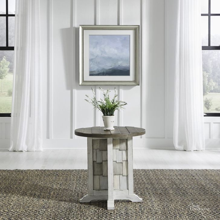 The appearance of River Place Round Chairside Table In Riverstone White and Tobacco designed by Liberty in the country / farmhouse interior design. This white piece of furniture  was selected by 1StopBedrooms from River Place Collection to add a touch of cosiness and style into your home. Sku: 237-OT1021. Product Type: Chairside Table. Material: Wood Veneer. Image1