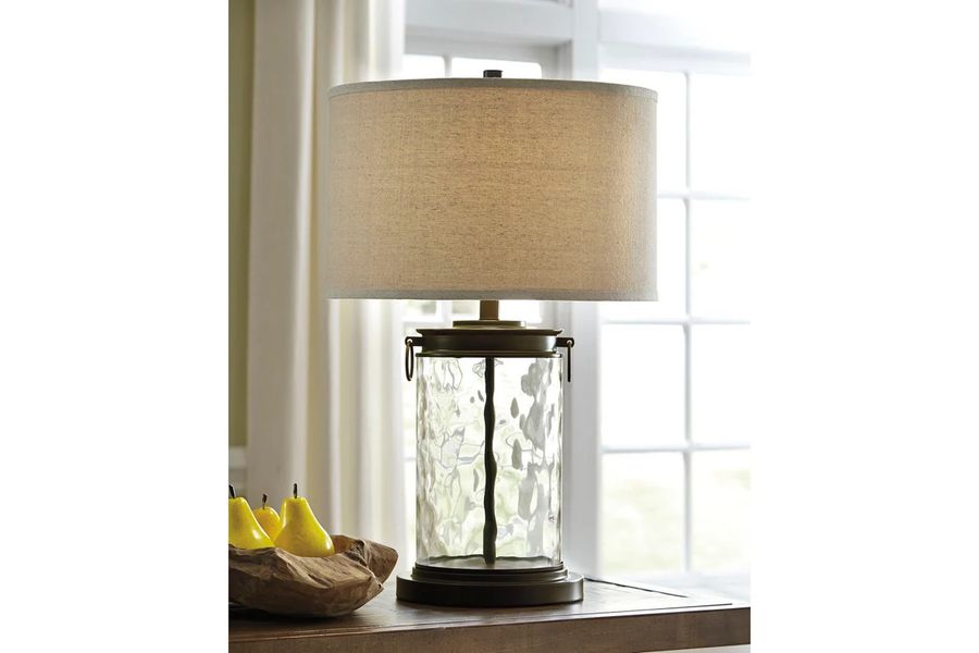 The appearance of Tailynn Clear and Bronze Glass Table Lamp designed by Signature Design by Ashley in the transitional interior design. This clear/bronze piece of furniture  was selected by 1StopBedrooms from Tailynn Collection to add a touch of cosiness and style into your home. Sku: L430324. Material: Glass. Product Type: Table Lamp. Image1